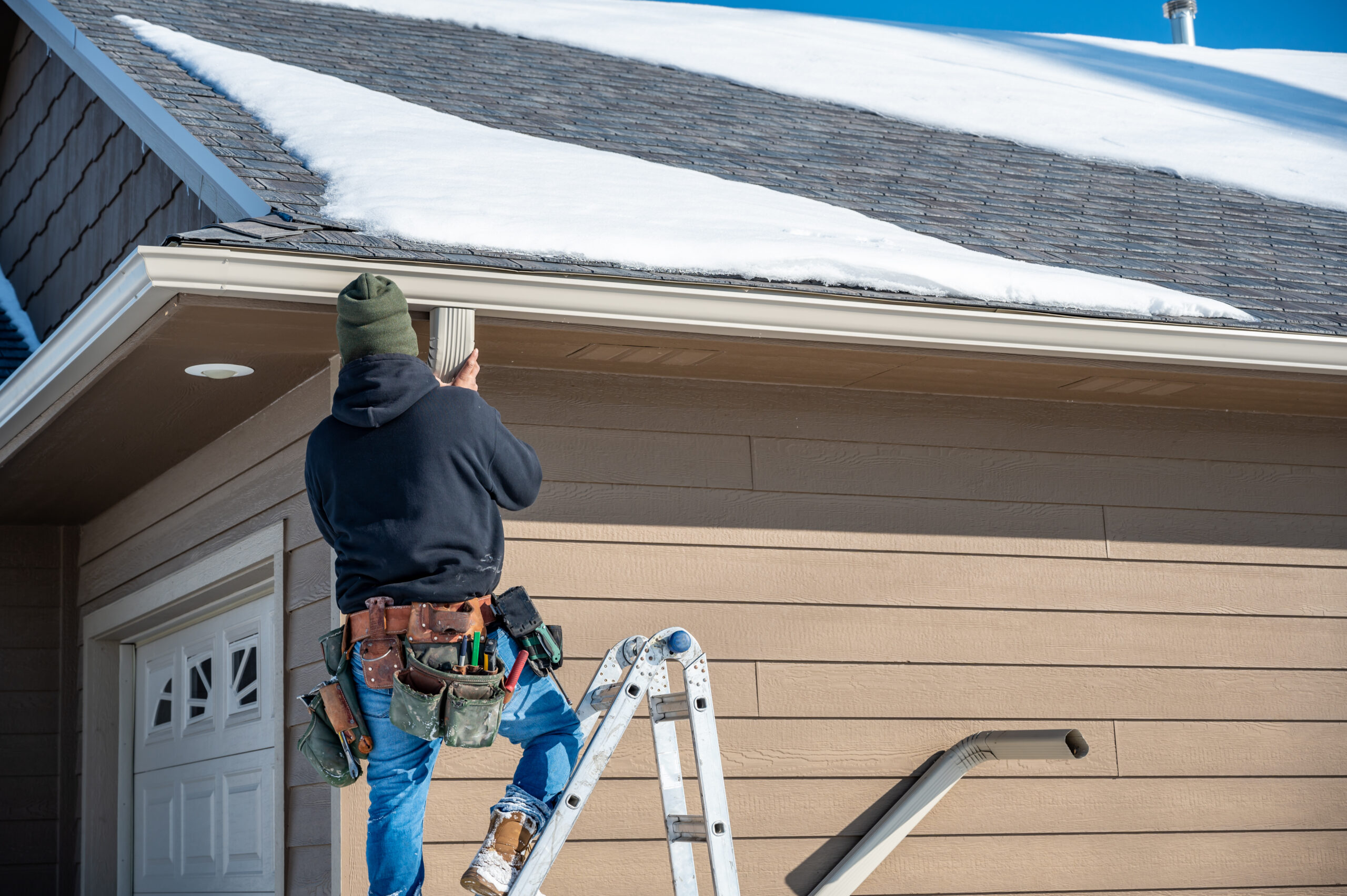 Contractor installing gutters on a residential building in the winter with snow on the roof. Seamless Gutter Installation